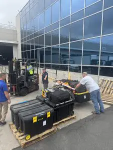 Trunks and carriage gear being unloaded curbside at the JFK cargo terminal with a forklift and cargo handlers
